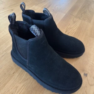 Svarta Uggs  - Säljer ett par svarta UGG boots i mocka. De är i mycket bra skick och perfekta för höst och vinter. Bootsens insida är mjuk och varm, vilket gör dem superbekväma. De har en stilren design med elastiska paneler på sidorna för enkel på- och avtagning. Kommer även med kartong endast använda en gång 