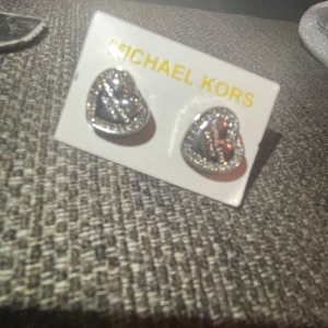 Hjärtformade örhängen från Michael Kors - Säljer ett par superfina hjärtformade örhängen från Michael Kors. De är i silverfärg och glittrar med små stenar runt kanterna. Perfekta för att ge en extra touch till din outfit, oavsett om det är till vardags eller fest. Kommer i originalförpackning.