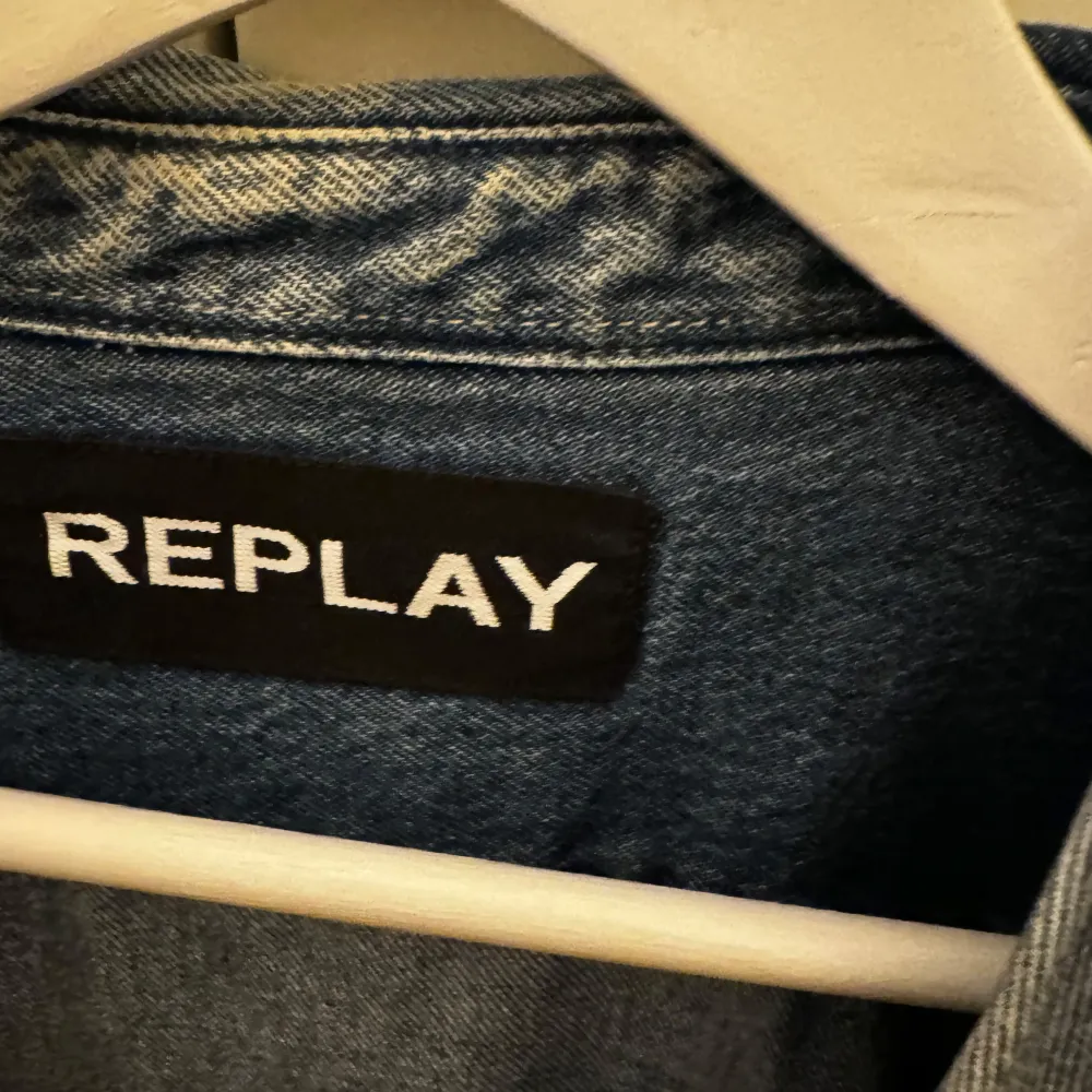 Säljer en snygg jeansjacka från Replay i klassisk blå denim. Jackan har en normal passform och långa ärmar. Den har två bröstfickor med lock och knappar. På baksidan finns Replay-loggan i stort tryck. Perfekt för vår och höst!. Takit.