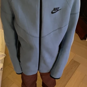 Ljusblå hoodie från Nike - Säljer en snygg ljusblå hoodie från Nike i storlek L. Den har en dragkedja framtill och två praktiska fickor. Perfekt för höst och vår, med en stilren design och Nike-logga på bröstet. Superbekväm och passar till både träning och vardag!