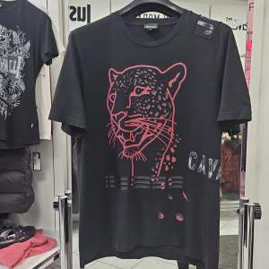 Snygg svart t-shirt från Just Cavalli i storlek S. Den har ett coolt pantermotiv i rosa och silver på framsidan. Perfekt för en avslappnad stil med en touch av attityd. Gjord i mjukt bomullsmaterial för extra komfort. T-shirt är stor i storleken. Motsvarar storlek M. T-shirt är I perfekt skick.