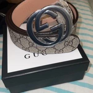 Gucci bälte med GG-mönster - Säljer ett snyggt Gucci bälte i nytt skick. Det har det klassiska GG-mönstret i beige och brunt, med ett stort silverfärgat GG-spänne. Perfekt för att lyfta vilken outfit som helst! Kommer i originalförpackning. Med kvitto 🧾 
