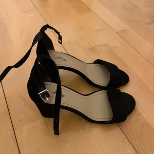 Svarta klackskor från Alley - Snygga svarta klackskor från Alley i mocka med en elegant rem runt ankeln. Använda en gång endast! Storlek 37.