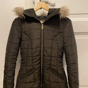 Mörkbrun dunjacka med pälskrage - Säljer en snygg mörkbrun dunjacka med pälskrage. Den är i mycket bra skick och har en figursydd passform. Köpte den på Sellpy för 400kr, men var för tight på mig. Ser lite grön aktig ut i färgen på kamera, men den är en mörkbrun färg. Fråga gärna om fler bilder!❄️💕