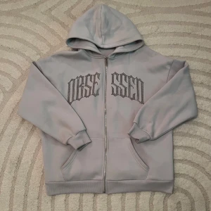 Grå blå hoodie med text - Säljer en grå hoodie med cool text på bröstet. Den har en dragkedja framtill och en skön luva. Perfekt för en avslappnad stil eller kyliga dagar. Passar både till vardags och chillkvällar.