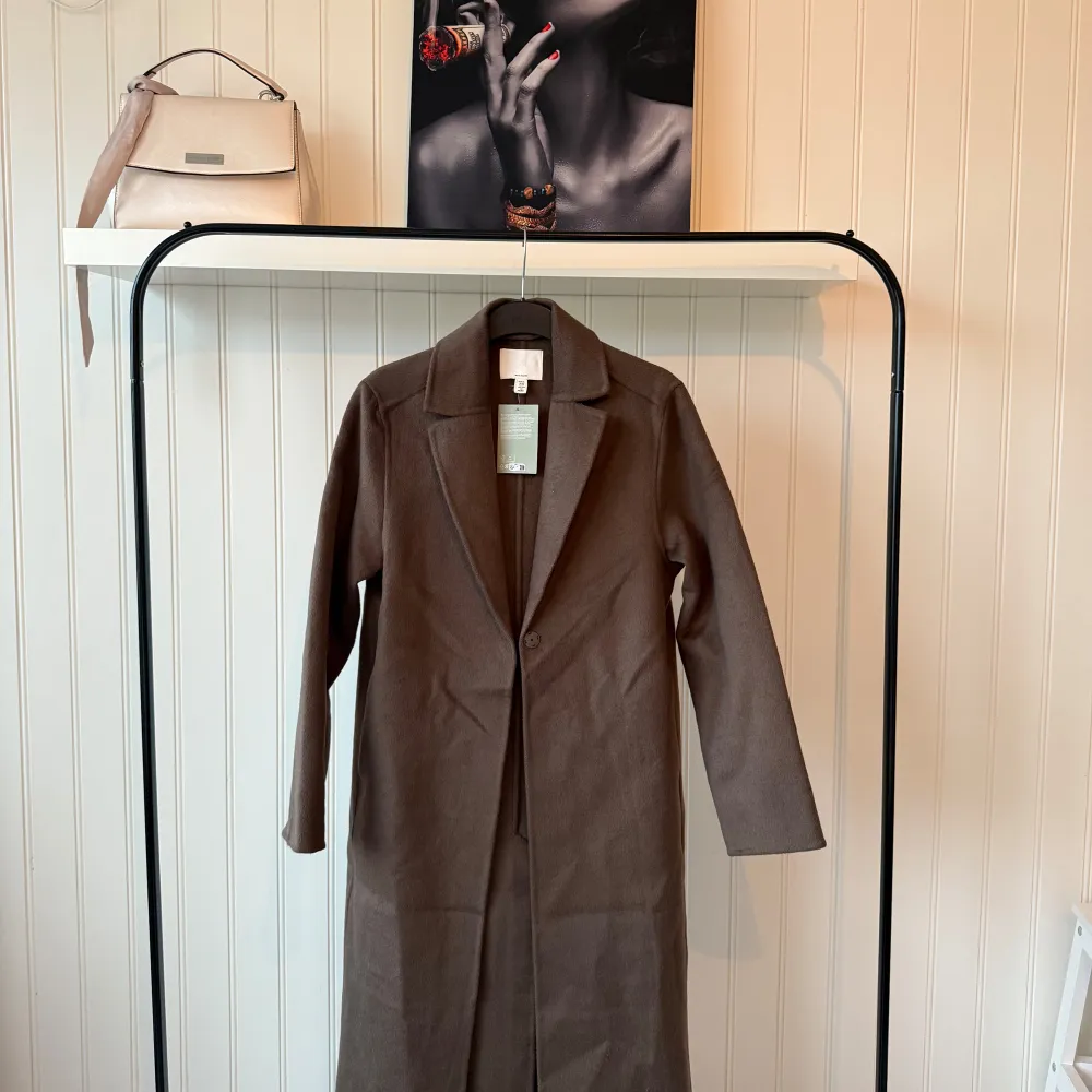Säljer en stilren brun kappa i mycket bra skick. Den har en klassisk design med långa ärmar och knappar framtill. Perfekt för höst och vår, och ger en elegant touch till vilken outfit som helst. Passar både till vardags och festliga tillfällen.. Takit.