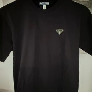 Prada t-shirt - Säljer en stilren svart t-shirt från Prada i mycket bra skick. Den har en klassisk passform med korta ärmar och ett diskret Prada-märke på bröstet. Perfekt för både vardag och fest. Obs: skriv innan köp!
