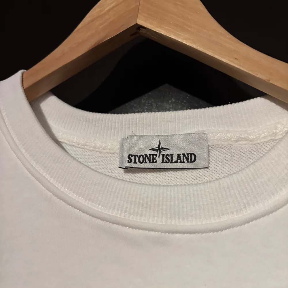 Säljer en stilren vit långärmad tröja från Stone Island. Den har en klassisk design med rund hals och det ikoniska märket på ärmen. Perfekt för både vardag och festliga tillfällen. Tröjan är i mycket bra skick och redo för en ny ägare!. Tröjor & Koftor.