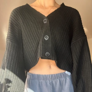 Svart ribbad kofta från Gina Tricot - Säljer en superfin svart ribbad kofta från Gina Tricot. Den är croppad med stora knappar framtill och har långa ärmar. Perfekt för höst och vår när du vill ha något stilrent och bekvämt. Passar både till vardags och fest! 🖤