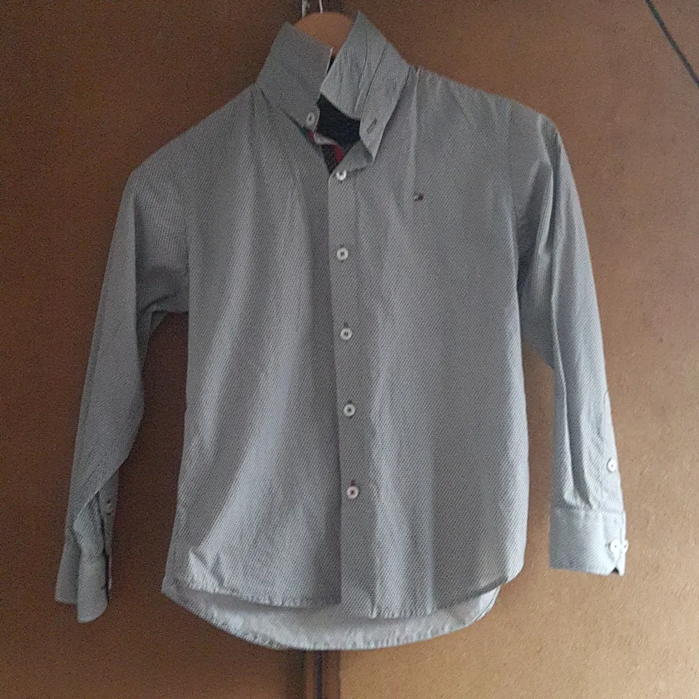 Snygg grå skjorta från Tommy Hilfiger i custom fit. Den har ett diskret prickigt mönster och klassiska knappar framtill. Perfekt för både vardag och fest! 👔. Paidat.
