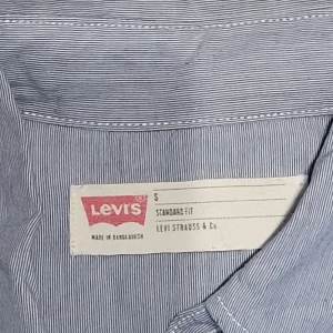 Blå randig skjorta från Levi's - Säljer en snygg blå randig skjorta från Levi's i storlek S. Skjortan har långa ärmar och klassisk krage med knappar hela vägen ner. Perfekt för både vardag och fest! 💙