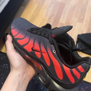 Nike tn svart röda  - Säljer ett par snygga Nike sneakers i svart och röd med coolt mönster. Skorna har en modern design med snörning och en bekväm passform. Perfekta för både vardag och träning. De är i mycket bra skick och redo för nya äventyr!