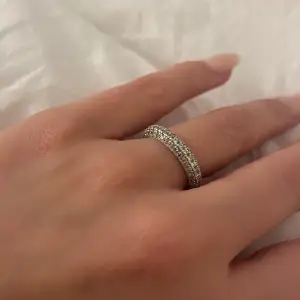 Säljer en superfin glittrig ring i silver. Den är täckt med små gnistrande stenar runt hela ringen, vilket ger en lyxig känsla. Perfekt för att piffa upp vilken outfit som helst! Passar både till vardags och fest. 💍✨