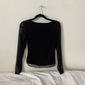 Svart långärmad topp - Snygg svart topp med långa ärmar i ett transparent material. Perfekt för en kväll ute eller en stilren vardagslook. Toppen har en enkel design med en lätt vågig kant nertill som ger en extra touch💋💋