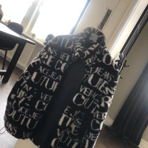 Svart och vit jacka från Versace Jeans Couture Nyskick! - Säljer en snygg och unik svart och vit jacka från Versace Jeans Couture. Jackan har ett iögonfallande mönster med text och är perfekt för att sticka ut. Den är långärmad och har en mysig, lite oversized passform. Perfekt för höst och vinter! Nyskick !
