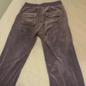 juicy couture lila mjukisbyxor med fickor  - Superbekväma lila mjukisbyxor i mjukt material. De har två praktiska fickor med knappar på baksidan. Perfekta för en avslappnad dag hemma eller en snabb tur till affären. Midjan är elastisk för extra komfort. Passar perfekt till en hoodie eller en enkel t-shirt. pris går att diskuteras!