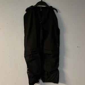 Svarta skidbyxor från Isbjörn of Sweden - Säljer ett par svarta byxor från Isbjörn i mycket bra skick. De är perfekta för vinteraktiviteter med sin robusta design och elastiska benslut. Byxorna har en praktisk dragkedja och knappar framtill. Perfekta för att hålla sig varm och torr under kalla dagar!