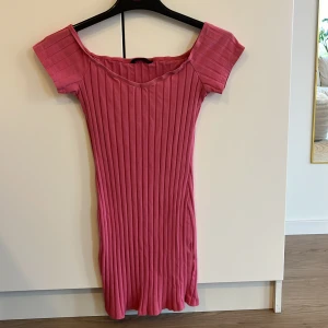 Ribbad rosa klänning - Säljer en superfin ribbad rosa klänning med offshoulder-design. Den är kortärmad och har en smickrande v-ringning. Perfekt för sommardagar eller en avslappnad fest. 