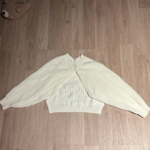 Vit stickad tröja med twistdetalj - Säljer en superfin vit stickad tröja med en unik twistdetalj framtill. Den har en croppad passform och långa ärmar, perfekt för höst och vinter. Tröjan är både stilren och mysig, idealisk för att hålla sig varm och trendig. Passar perfekt till både jeans och kjol!