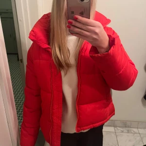 Röd pufferjacka - Säljer en snygg röd pufferjacka i mycket bra skick. Jackan har en dragkedja framtill och är perfekt för kyliga dagar. Den är långärmad och har en hög krage för extra värme. Passar perfekt för höst och vinter! Säljer då den inte längre kommer till användning. Köpte för 800 men har inte använts mycket då jag var bortrest under vintersäsongen 