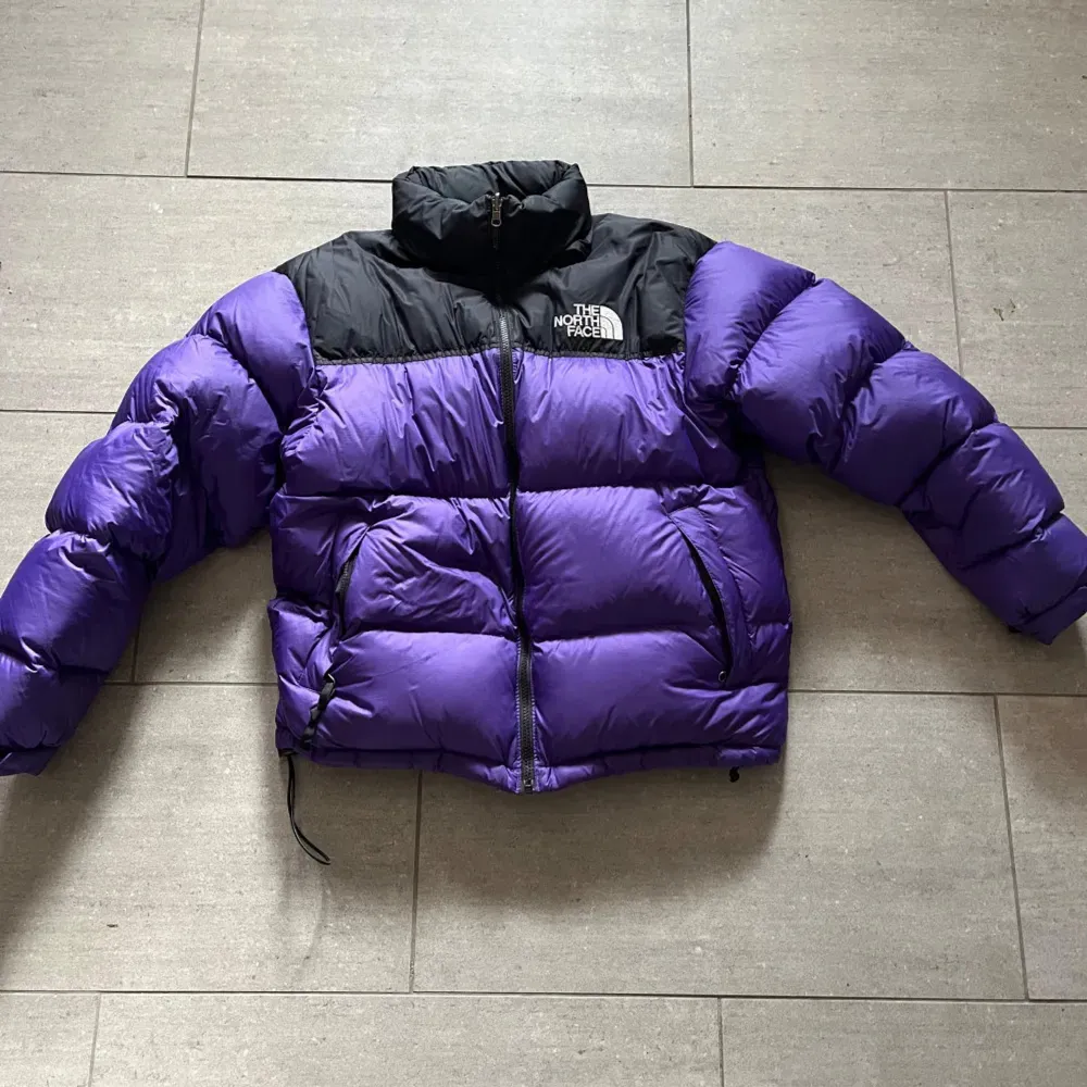 Säljer en snygg och varm lila dunjacka från The North Face med svarta detaljer. Jackan har en dragkedja framtill och är perfekt för kalla vinterdagar. Den är i mycket bra skick och har långa ärmar. Perfekt för både vardag och äventyr!. Jackor.