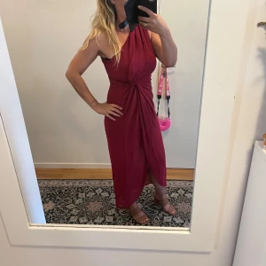 Vinröd oneshoulder klänning - Snygg vinröd oneshoulder klänning med en elegant omlott-design och knytning i midjan. Perfekt för festliga tillfällen! Klänningen har en smickrande passform och är gjord i ett mjukt material som faller fint.Helt ny