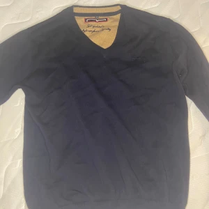 V ringad tröja  - Säljer en stilren mörkblå tröja som är v ringad. Perfekt för både vardag och fest mm. Tröjan har en broderad logga på bröstet och är i mycket bra skick. Bara att skriva för mera bilder elr info👍🏼