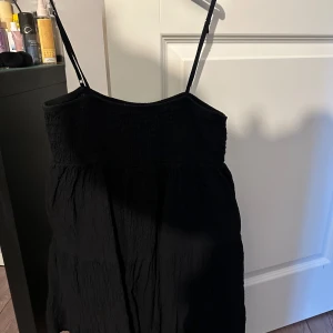 klänning från Zara - Säljer en stilren svart klänning från Zara i storlek M. Klänningen har smala axelband och en smockad överdel som ger en bekväm passform. Perfekt för både vardag och festliga tillfällen. Tillverkad i ett mjukt och lätt material. Den är aldrig använd och är helt som ny.