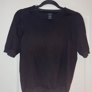 Svart tröja från Lindex - Säljer en stilren svart tröja från Lindex i storlek XS. Tröjan har korta ärmar och är perfekt för både vardag och fest. Den är i bra skick och passar till alla tillfällen. Enkelt att matcha med olika outfits!