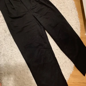 Svarta byxor - Säljer ett par stilrena svarta byxor i mycket bra skick. De har en hög midja och stängs med en knapp och dragkedja. Perfekta för både vardag och fest!