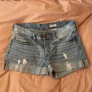 Säljer ett par snygga blå jeansshorts från H&M i storlek M. De har en loose fit med låg midja och är perfekt slitna för en avslappnad look. Shortsen har upprullade kanter och klassiska femficksdetaljer. Perfekta för sommardagar eller festivalhäng!