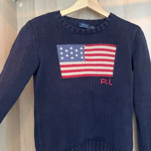 Mörkblå stickad tröja från Ralph Lauren - Snygg marinblå stickad tröja från Ralph Lauren med en flagga. Bra skick. Så snygg, passar till allt!💕💕