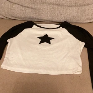 Svartvit croppad topp med stjärna - Säljer en cool svartvit croppad topp med en stor svart stjärna på framsidan. Toppen har långa svarta ärmar och en vit kropp, perfekt för en avslappnad och trendig look. 