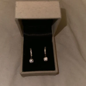Silver creoler med kubisk zirkonia  - Små fina creoler med kubiska zirkoner och ett litet gnistrande hänge. Ena örhänget har tappat 2 stenar men de är annars i bra skick och ask medkommer