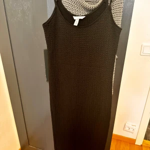 Svart ärmlös klänning från H&M - Säljer en stilren svart ärmlös klänning från H&M. Den är i storlek M och har en tight passform som framhäver figuren. Perfekt för både vardag och festliga tillfällen. Klänningen är i ett bekvämt material som känns skönt mot huden.