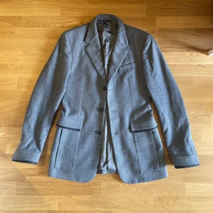 Jil Sander sample kavaj/kappa - Meiers familjen era Sample Jil Sander kavaj ifrån 2017. Svarta detaljer runt ficka, krage och ärmslut. Nedarsta knappen är lite förstörd men annars riktigt bra skick. Extremt bra kvalite längre kavaj/kappa Size 48/medium, gjord i italien