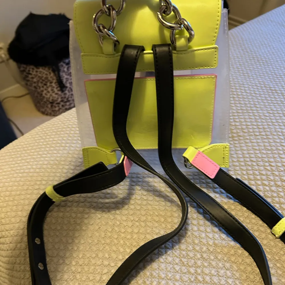 Säljer en supercool transparent ryggsäck från Tommy Hilfiger med neongula detaljer. Den har en unik design med en svart spänne framtill och justerbara svarta axelremmar. Perfekt för att ge din outfit en färgklick! 🖤💛 Nyskick . Väskor.