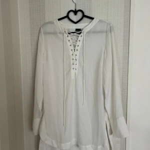 Vit blus ifrån Gina Tricot  - Vit blus med snörning framtill. Blusen har långa ärmar och en något längre baksida.