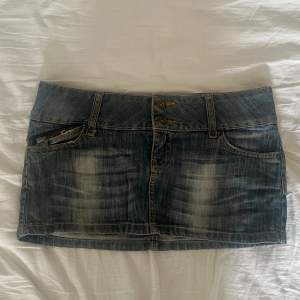 Säljer en cool låmidjad jeanskjol från SNG Jeans i storlek M. Den är i en klassisk blå denimfärg med slitna detaljer. Kjolen har två knappar fram och dragkedjor både fram och bak. Perfekt för en vanlig dag eller en utekväll! 💗