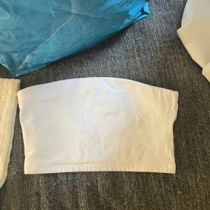 Vit tubtopp - Säljer en enkel och stilren vit tubtopp. Den är axelbandslös och har en tight passform som sitter bra på kroppen.