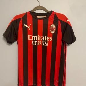 AC Milan fotbollströja från Puma - Säljer en AC Milan fotbollströja från Puma i klassiska röd-svarta ränder. Tröjan har korta ärmar och är i nyskick. Den är tillverkad i ett lätt och andningsbart material med DryCell-teknologi för att hålla dig torr och bekväm under matchen.
