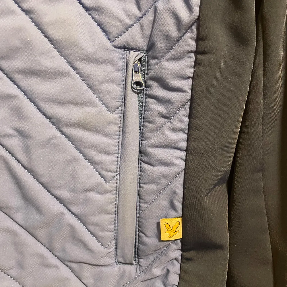 Säljer en snygg blå quiltad jacka från Lyle & Scott. Jackan har en dragkedja framtill och ett coolt mönster. Den är perfekt för höst och vår med sina långa ärmar och bekväma passform. Detaljer som den gula loggan på bröstet ger den en extra touch. Perfekt för både vardag och fest!. Jackor.