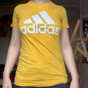 Säljer en snygg gul t-shirt från Adidas med deras klassiska logga i vitt på bröstet. T-shirten är kortärmad och har en normal passform. Perfekt för vardagsbruk eller träning!