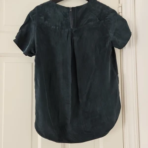 Mörkgrön kortärmad topp - Säljer en stilren mörkgrön topp med korta ärmar. Toppen har en rund hals och en dragkedja i ryggen för enkel påklädning. Perfekt för både vardag och fest!