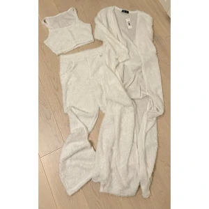 Vit mysig set med lång kofta - Supermysigt vitt set som består av en lång kofta, ett croppat linne och byxor. Perfekt för en chill dag hemma eller en mysig kväll. Setet är gjort i ett fluffigt och mjukt material som känns som att ha på sig ett moln.