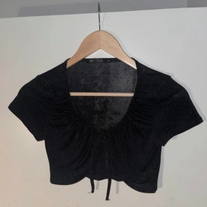 Svart glittertopp med knytning - Oanvänd, säljes pga kommer ej till användning. Croppad glittrig topp i skönt material, superfint över tex en bikini eller bandeutopp🫶  Normal i storleken🖤