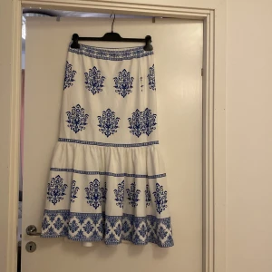 Vit och blå långkjol från Shein - Säljer en superfin vit långkjol från Shein med blått mönster. Kjolen har ett vackert tryck med detaljerade blå mönster och en volangdetalj längst ner. Perfekt för sommardagar eller en avslappnad fest. Den är i storlek XL och i nyskick!