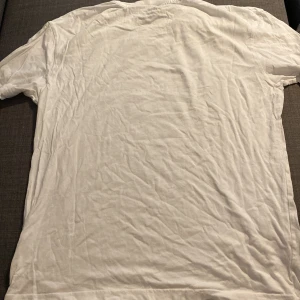 Vit t-shirt från Stones Apparel Co - Säljer en vit t-shirt från Stones Apparel Co med ett coolt tryck av en orm och texten 'Hand Made Original Classics' och 'Registered Trademark Since 1917'. Perfekt för en avslappnad stil. T-shirten är kortärmad och i bomull, vilket gör den skön att ha på sig. Lite skrynklig men säljer den för billigt så en tvätt och kanske ett strykjärn göt jobbet👍