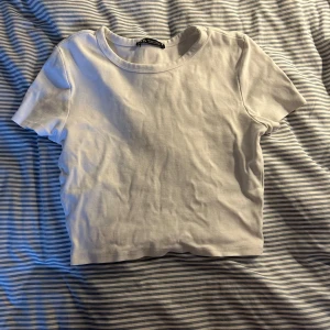 Vit croppad t-shirt - Säljer en enkel och stilren vit croppad t-shirt. Perfekt för sommardagar eller som ett basplagg i garderoben. T-shirten har korta ärmar och är i ett mjukt bomullsmaterial. Passar bra till jeans eller kjol för en avslappnad look.