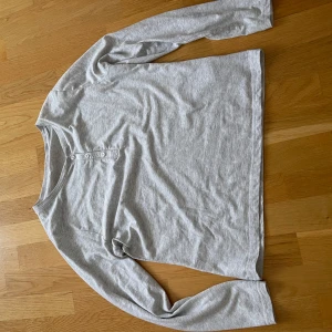 Grå långärmad tröja från Cubus - Säljer en enkel och bekväm grå långärmad tröja från Cubus. Den är gjord av 60% bomull och 40% polyester, vilket gör den mjuk och skön att ha på sig. Tröjan har en knappdetalj framtill som ger den lite extra stil. Perfekt för vardagsbruk!